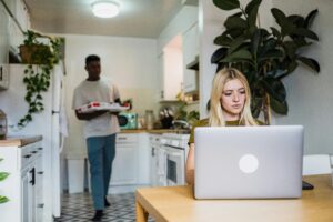 A couple multitasking with work and leisure in a cozy home kitchen setting.